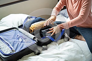 Happy young woman hands packing clothes into travel luggage on bed at home or hotel room for a new journey. Â Tourism and vacation